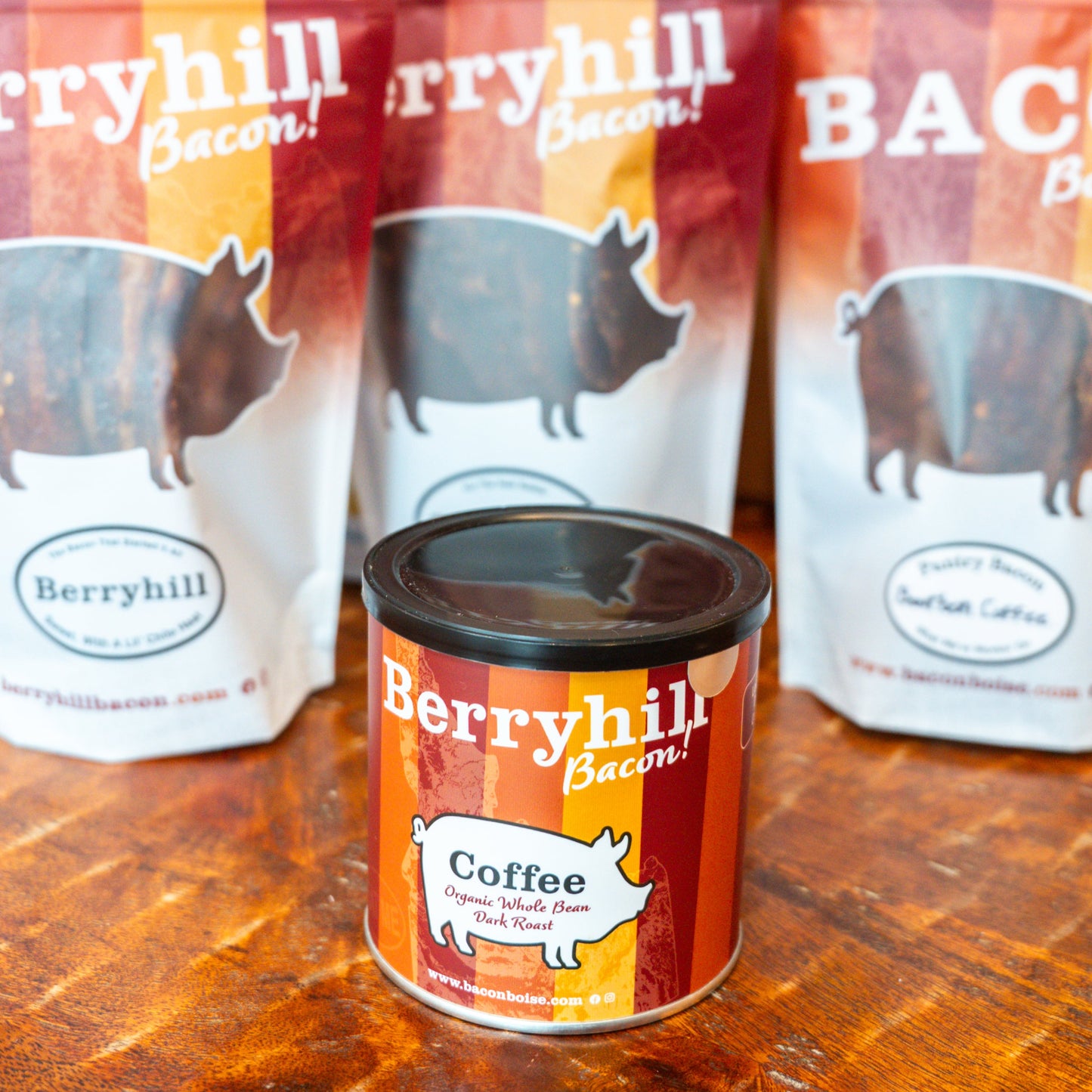 A can of Berryhill Coffee with the label facing forward, with two packages of Berryhill Bacon blurred in the background.