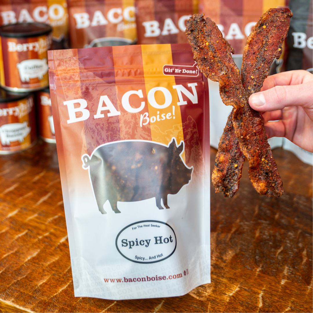 A packaged product labeled 'BACON Boise! Spicy Hot' with a picture of a pig and people holding strips of spicy hot bacon.