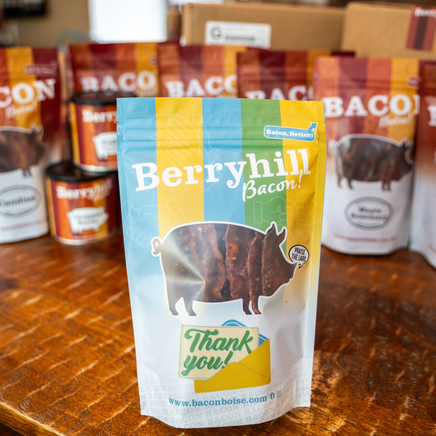 A pack of Berryhill Bacon with a 'Thank You' card design on the front, placed on a wooden surface with additional packs blurred in the background.