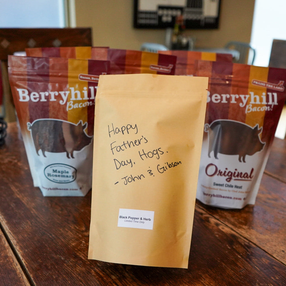 Bags of berryhill bacon on a wooden table with a personalized card.