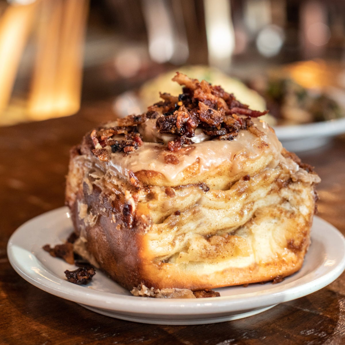 Cinnamon roll with chopped bacon on a plate in a restaurant setting