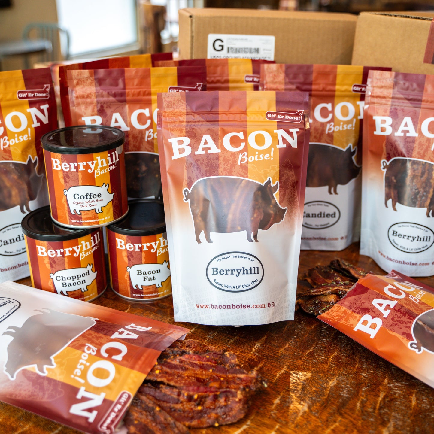 Assortment of Berryhill Bacon products including packaged bacon bags and canned items displayed on a wooden surface with 'BACON Boise' branding.