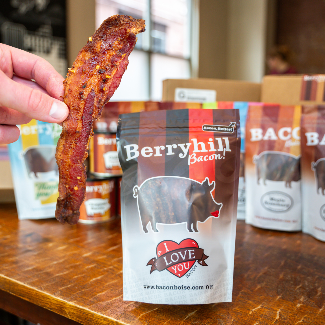 A packaged product labeled 'Berryhill Bacon' with the text 'I LOVE YOU' and a heart symbol, held by a hand, with additional packages in the background.