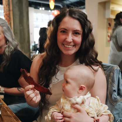 Woman holding a baby and a piece of bacon indoors