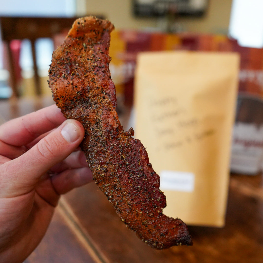 Hand holding a piece of seasoned meat with a blurred background