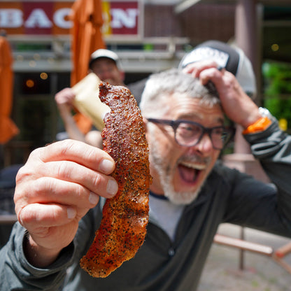 Man holding a large piece of seasoned meat outdoors with a building in the background