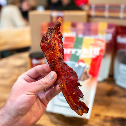 Hand holding a piece of bacon with a blurred background