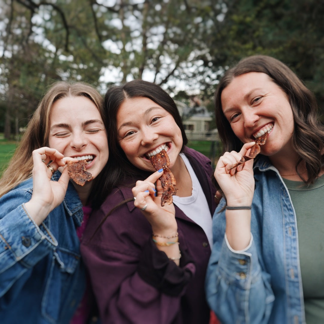 Three women eating bacon outdoors in a park