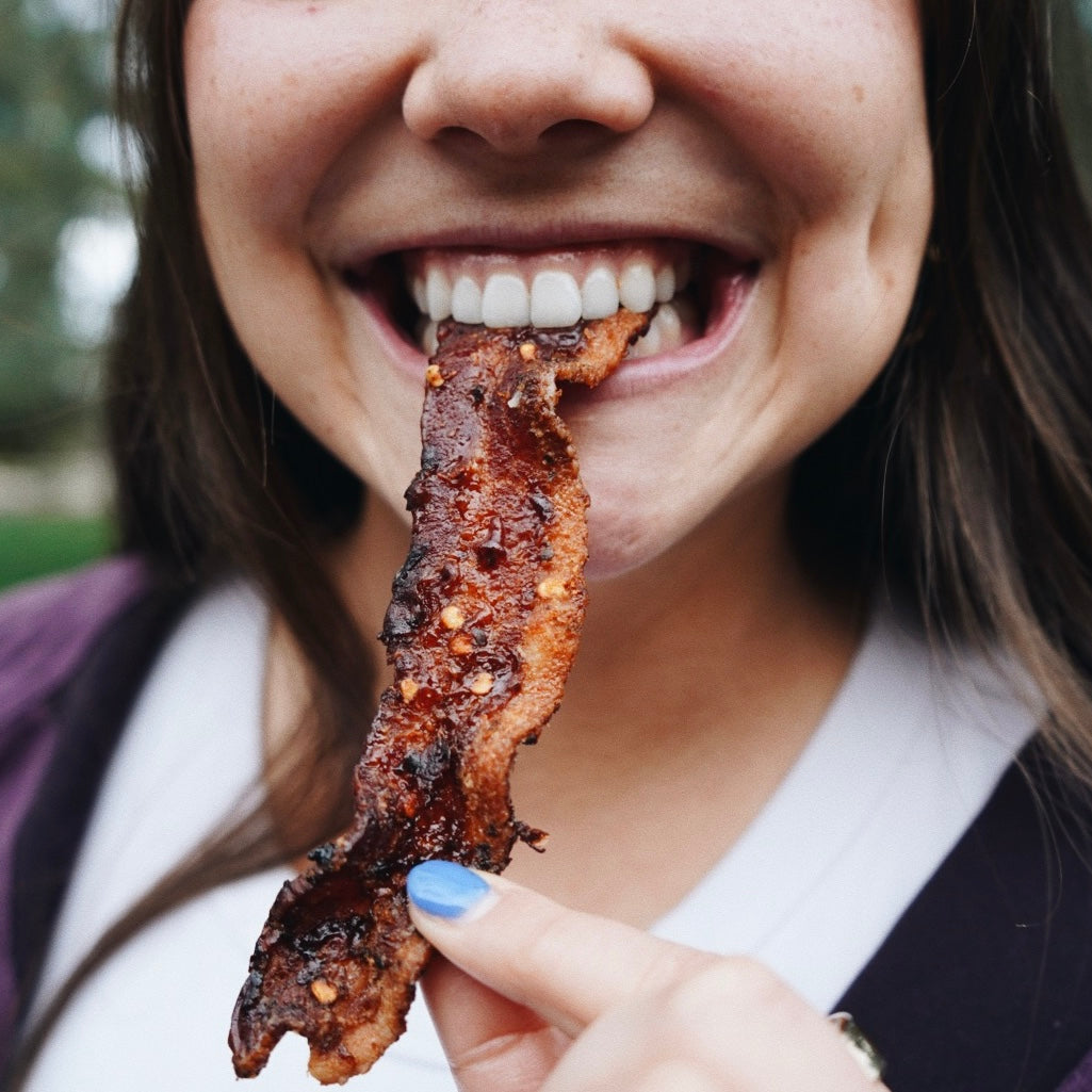 Person eating a piece of bacon outdoors