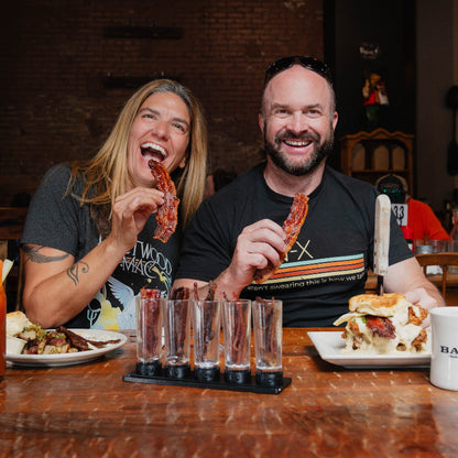 Two people enjoying food and drinks at a restaurant, with a focus on bacon-themed items.